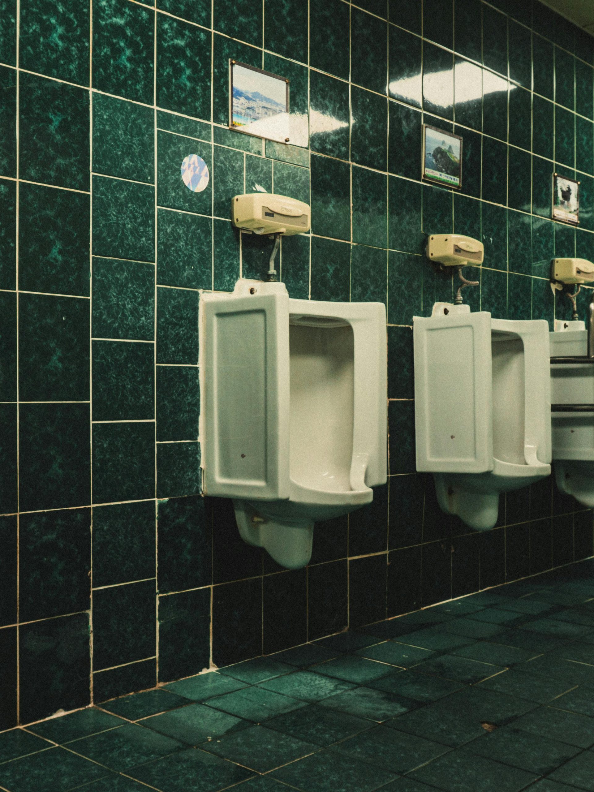 Three white ceramic urinals on green tiled wall in public restroom.